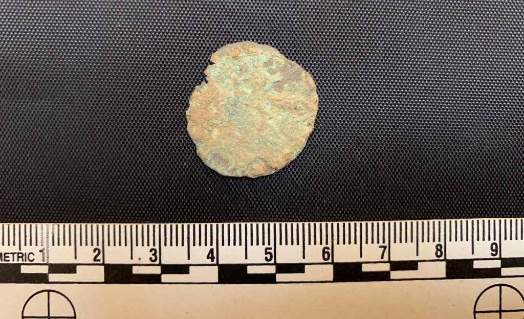 A close up of a badly-corroded copper coin with scale